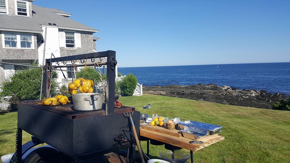 An outdoor grill with lemons set up on a seaside lawn overlooking the ocean