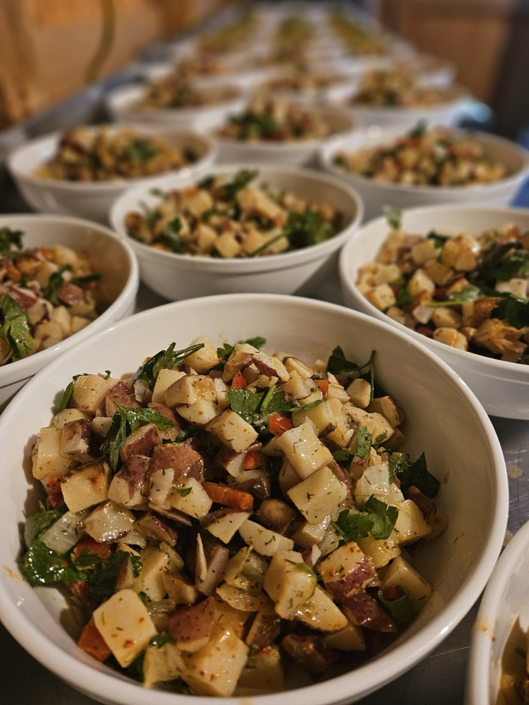 Rows of family-style bowls of potato salad with greens